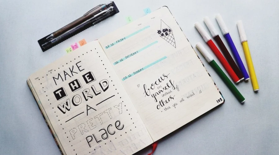 Imagem mostra caderno de notas com a frase Make The World A Pretty Place em fontes variadas escrito à mão