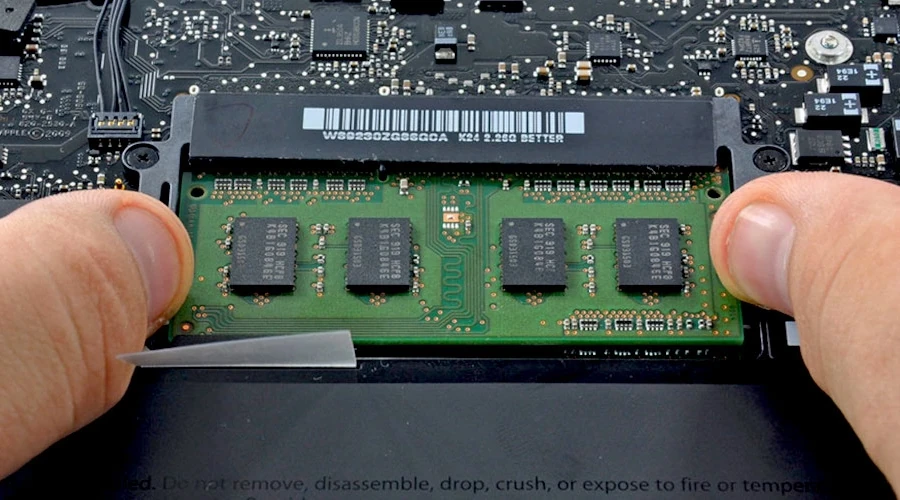 Pente de memória RAM sendo inserido na traseira de um notebook
