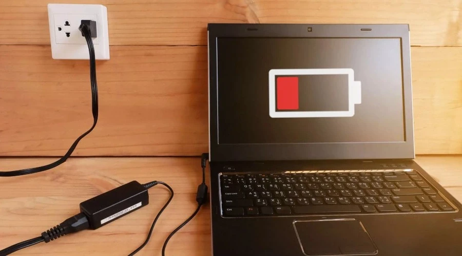 Notebook plugado na tomada mostrando um ícone de bateria fraca na tela