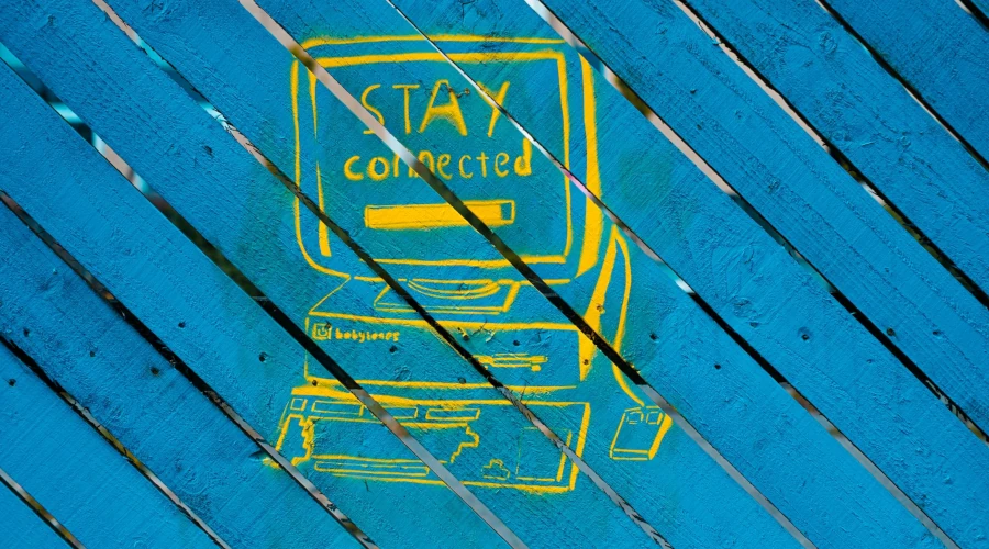 cerca de madeira azul claro com uma pixação de um computador amarelho e a tela dizendo stay connected