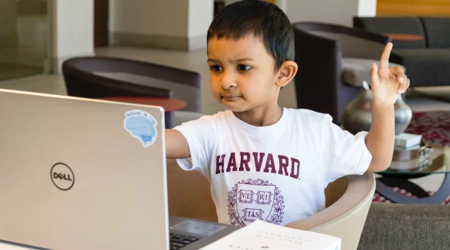 Menino usando camisa da Universidade de Harvard sentando em frente a um computador