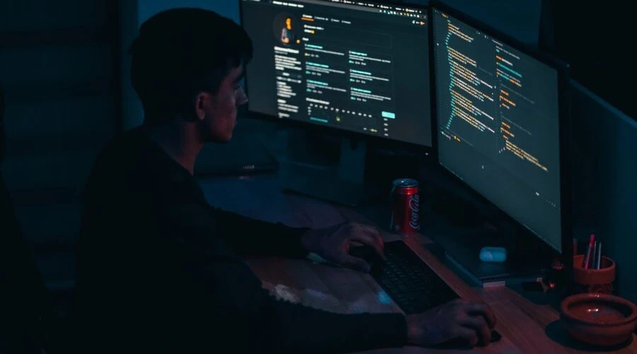 Programador escrevendo código na frente de duas telas, uma delas mostrando uma página do github aberta no navegador
