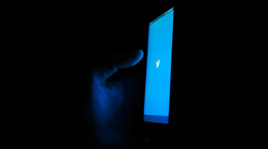 sala escura com uma mão segurando um celular e o aplicativo do twitter aberto