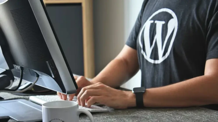 Homem digitando em um teclado em frente a um computador usando uma camisa com a marca do WordPress