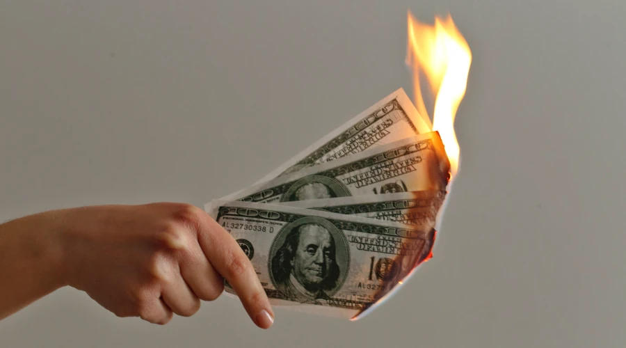 Mão feminina segurando quatro notas de cem dólares pegando fogo