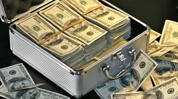 maleta de dinheiro com muito dólares aberta sobre uma mesa com várias cédulas espalhadas