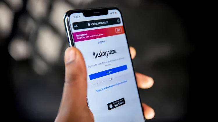 Mão masculina segurando um iPhone com o site do Instagram aberto no navegador Safari