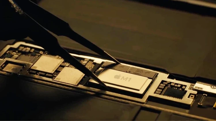 Foto de um chip Apple M1 sendo retirado de um MacBook com uma pinça