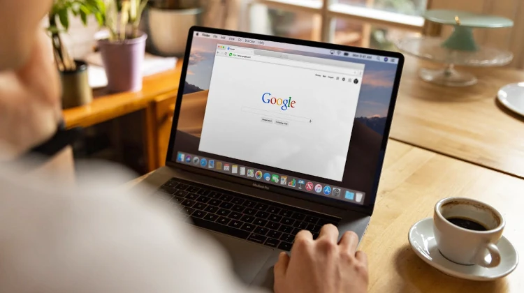 Homem tomando café de frente para MacBook com página da busca do Google aberto