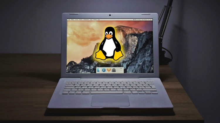 MacBook antigo sobre uma mesa com o Tux, mascote do Linux, em sua tela