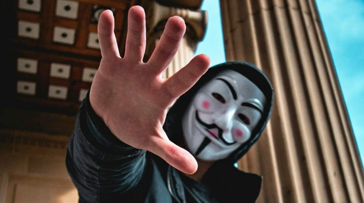 homem usando capuz e máscara do grupo hacker anonymous e esticando a mão na direção da câmera