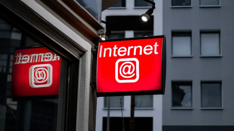 Entrada de cibercafé com uma placa indicando Internet e um @ num letreiro luminoso vermelho