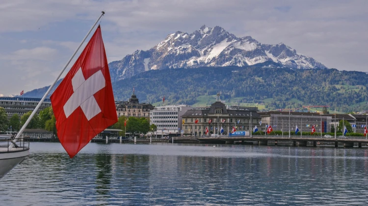 Bandeira da Suíça hasteada em um lado em frente a uma cidade próxima de uma montanha nevada