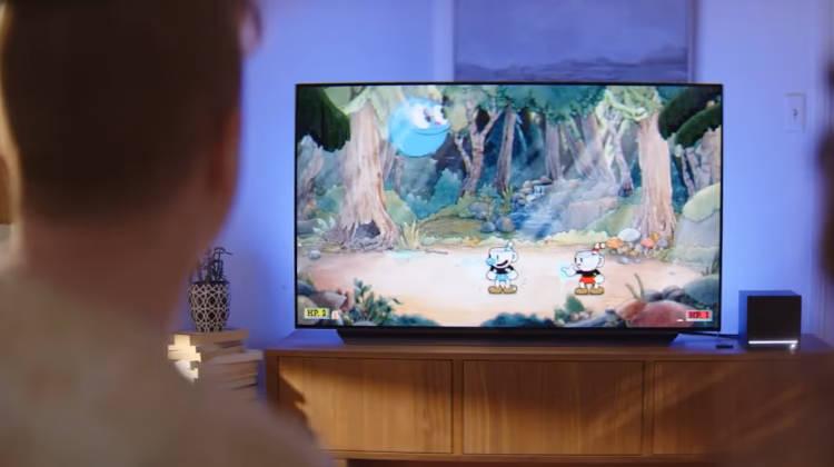 Foto de uma mulher de costas, jogando um jogo de videogame em uma televisão com um console Steam Machine ao lado