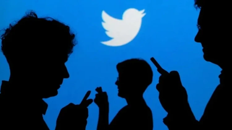 Sombras de pessoas segurando smartphone perto do rosto com logo do Twitter ao fundo