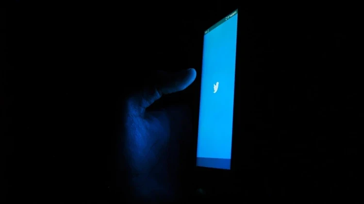 sala escura com uma mão segurando um celular e o aplicativo do twitter aberto