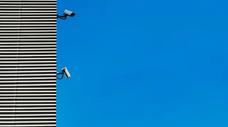 Quina de prédio com duas câmeras de segurança contra um céu azul ao fundo