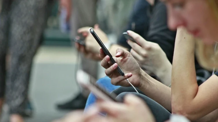 Close de várias pessoas segurando celulares sentadas em bancos de praça