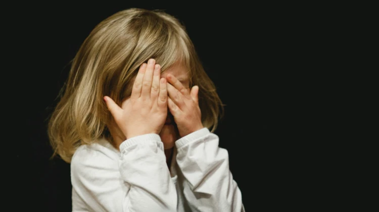 Menina loira cobrindo o rosto com as mãos em um fundo preto