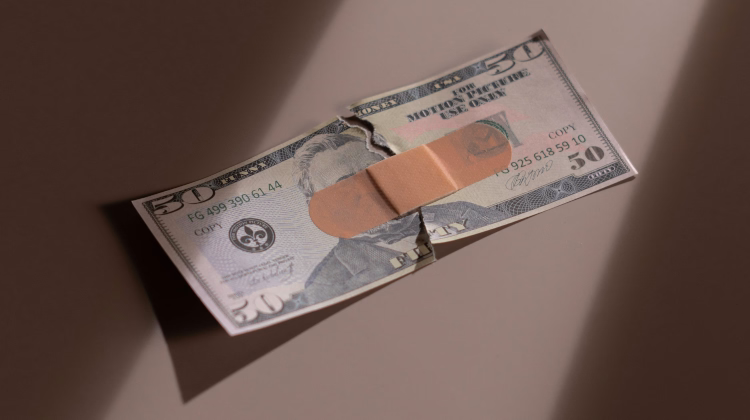Foto de uma nota de 50 dólares rasgada ao meio, no chão, com as duas metades unidas por um band-aid